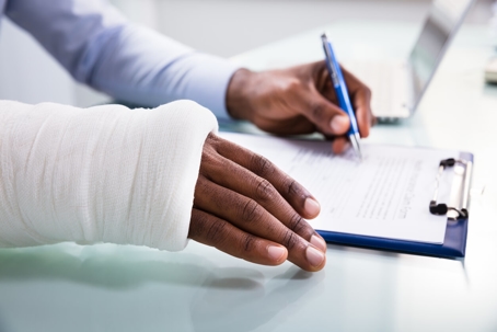 Person in a cast signing paperwork on a clipboard