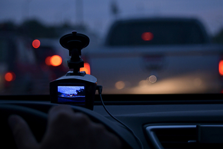 The DVR screen, on the car, fragment of the hand on the steering wheel, fixing the zero speed of the stopped car. On the road, during traffic jams, among other cars. In the evening, rush hour.
