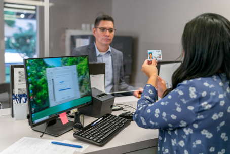 A female bank teller checks the personal identification of a male customer who is seeking to withdraw money from his bank account. Selective focus on the woman's hand as she holds the man's driver's license
