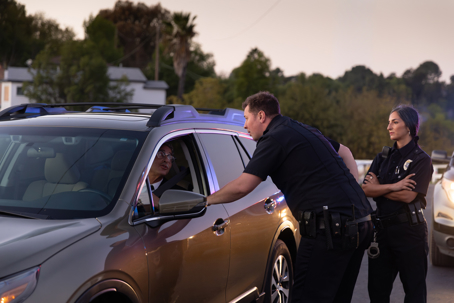 Shot of two police officers and a driver they pulled over on a scenic road at sunset.